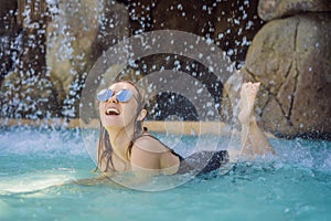 Young joyful woman under the water stream, pool, day spa, hot springs