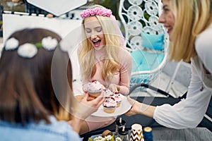 Young joyful women on a bachelorette party enjoying cupcakes with frosting, sitting outdoors on a sunny day