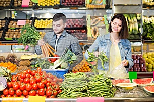 Young joyous couple choosing vegetables in grocery shop