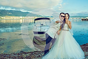 Young just married couple standing near the boat at the seaside in wedding dress and suit.