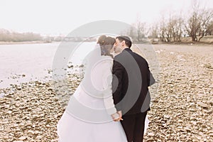 Young just married couple walking back kissing on the river coast