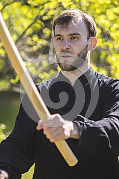 A young karate guy is engaged in Wushu with weapons in the Park. Practicing self-defense with sticks