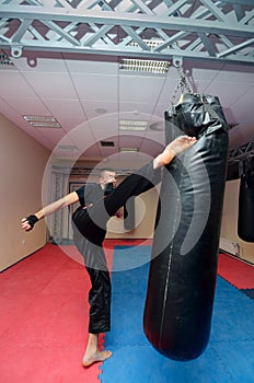 Young kickboxer kicking punching bag in sport gym