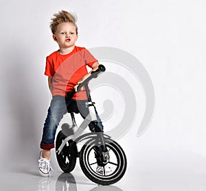 Young kid boy in orange t-shirt and blue jeans imagines he rides fast his new cool bicycle without pedals. Imitates engine sound