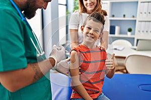 Young kid getting vaccine at doctor clinic smiling happy and positive, thumb up doing excellent and approval sign