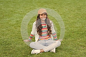 Young kid. Happy kid sit on green grass. Female child. Childhood and girlhood. School age