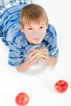 Young kid laying on the floor holding an apple.