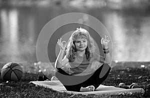 Young kid practicing yoga outdoors, lotus pose yoga. Harmony and meditation concept. Healthy lifestyle. Kid meditating
