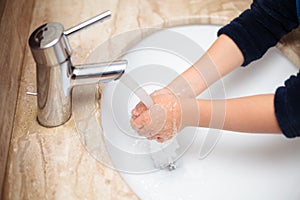 Young kid washing hands under tap water