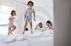 Young kids, jump and parents on bed with playing, game and excited in family house in morning. Naughty sibling children