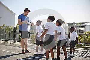 Young kids in a school playground with teacher holding ball