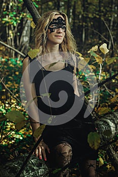 A young kind witch in a black dress with a black mask in a mystical forest in various poses. Art processing