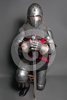 A young knight in medieval armor with a weapon in his hands kneeled