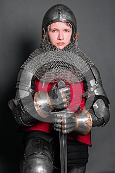 A young knight in medieval armor with a weapon in his hands kneeled