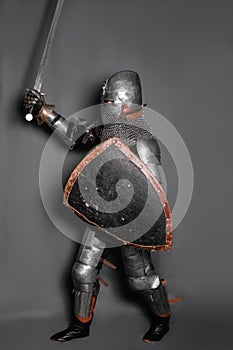 A young knight in medieval armor with a weapon in his hands kneeled