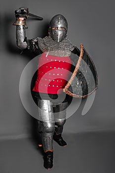 A young knight in medieval armor with a weapon in his hands kneeled