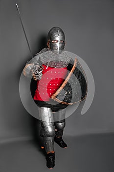 A young knight in medieval armor with a weapon in his hands kneeled