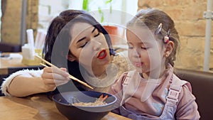 Young korean feeds her little daughter with a noodles in restaurant