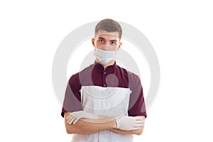 Young lab technician with a mask on his face worth gloved hands clasped