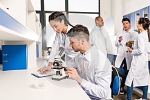 Young lab technicians working with microscope and taking notes on analysis