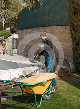 Young labourer working on a pool in a family house with a wheelbarrow and shovel