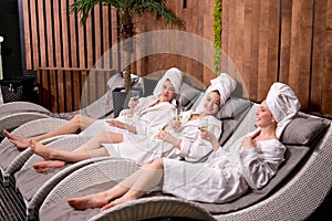 Young ladies enjoy drinking champagne at spa. Three beautiful women wearing bathrobes having cool resting, holidays
