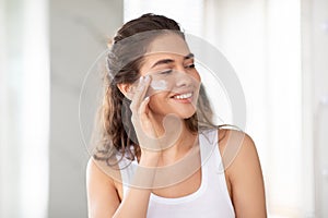 Young Lady Caring For Skin Applying Moisturizer Cream At Home