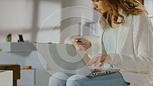 Young lady checking balance on bank account using laptop, card