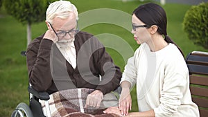 Young lady comforting depressed senior male in wheelchair, psychological crisis