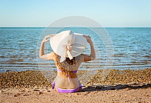 Young lady with curly hair and hat sitting on sand