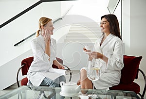 Young lady discussing skin care treatment with beautician while enjoying tea