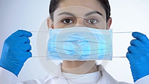 Young lady doctor putting on surgical mask, safety while examining, closeup photo