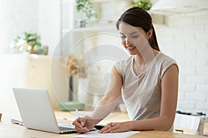 Young lady doing paperwork using laptop and calculator