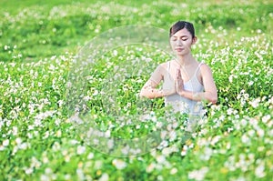 Young lady doing yoga exercise in green field with small white flowers outdoor area showing calm peaceful in meditation mind