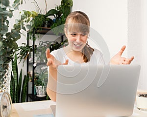 Young lady explaining things online on computer sitting at balcony full of plants