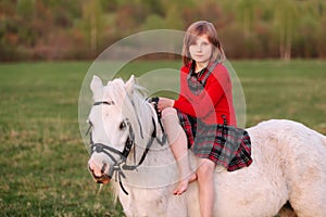 Young lady girl in red dress sitting on a white pony