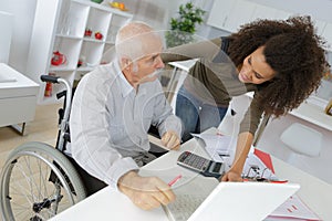 Young lady helping wheelchair bound man to use computer