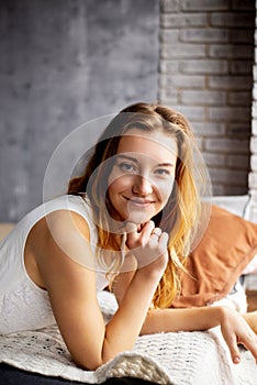 A young lady, her long hair cascading, lounges on a pillow in a white shirt, embodying tranquility and serenity