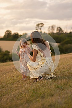 A young lady holding her little daughter in a field at sunset