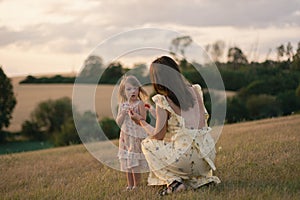 A young lady holding her little daughter in a field at sunset