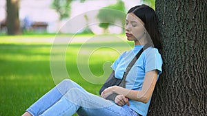 Young lady with injured arm in supporting sling sitting tree in park, medicine