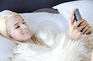 Young lady laying on a bed smiling and looking at her cell phone