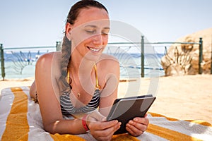 Young lady lounging and reading book in the shadow at the beach