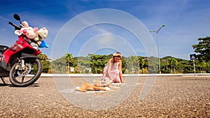 Young lady in pink dress squats and draws on asphalt