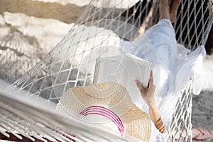 Young lady reading a book in hammock on tropical sandy beach.