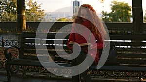 Young lady is reading a book, red head lovely girl is sitting on park bench, autumn colourful scene, lens flares, relax