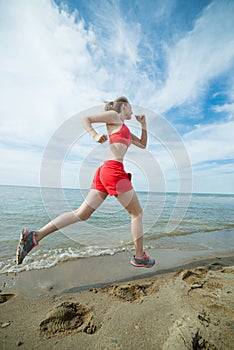 Young lady running at the sunny summer sand beach. Workout. Jog