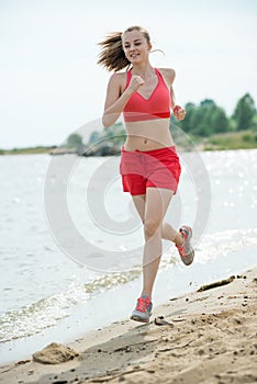 Young lady running at the sunny summer sand beach. Workout. Jog