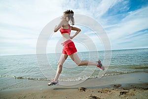 Young lady running at the sunny summer sand beach. Workout. Jog