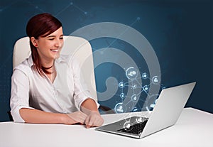 Young lady sitting at desk and typing on laptop with social network icons